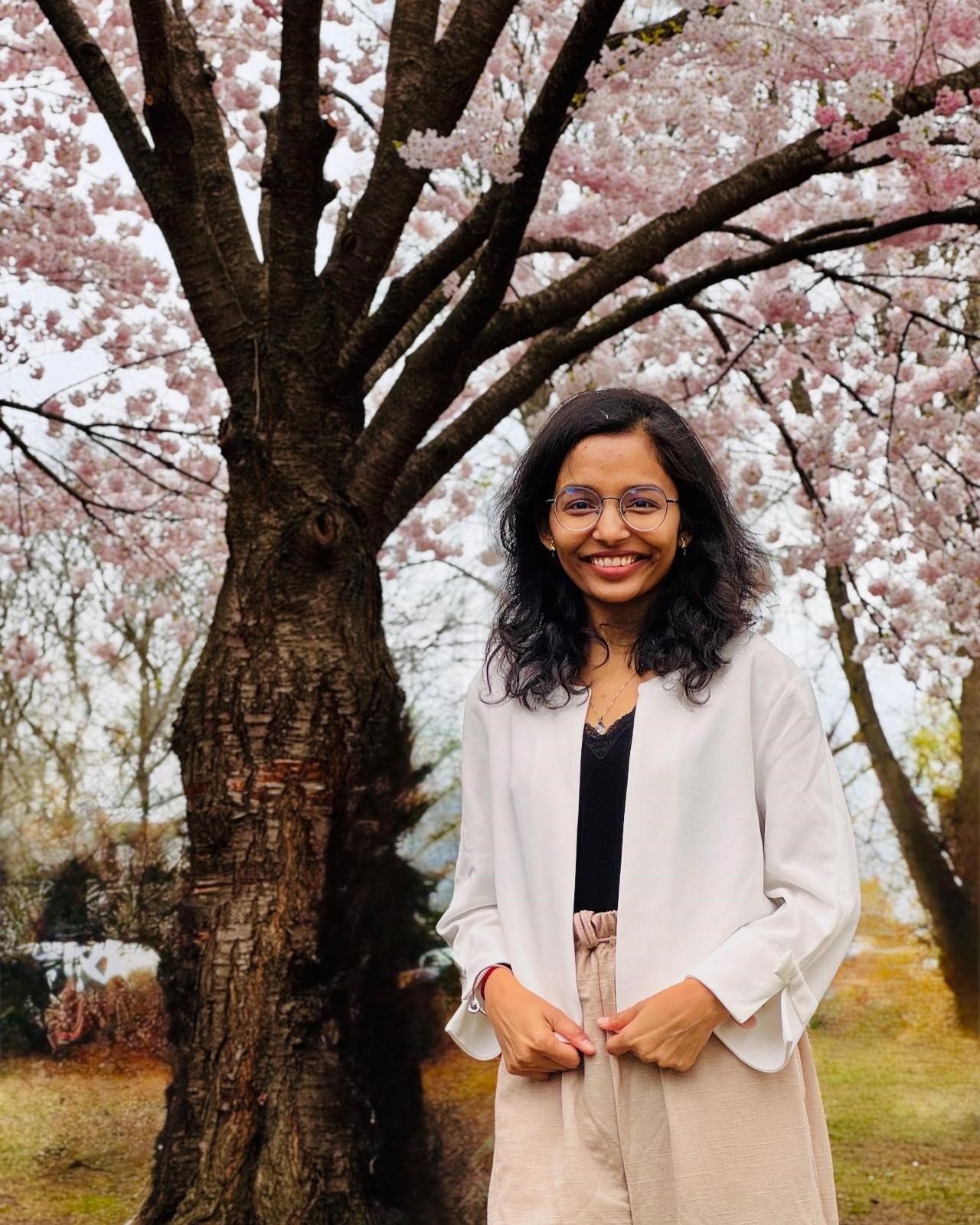 Smiling woman in white jacket stands near blooming cherry blossom tree
