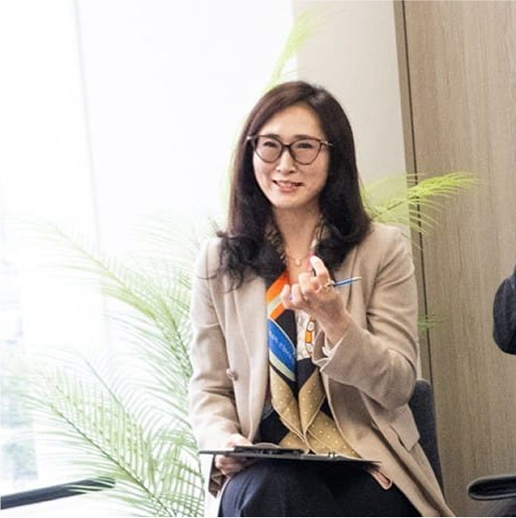 Businesswoman in beige blazer, holding a pen and notepad, smiling confidently.